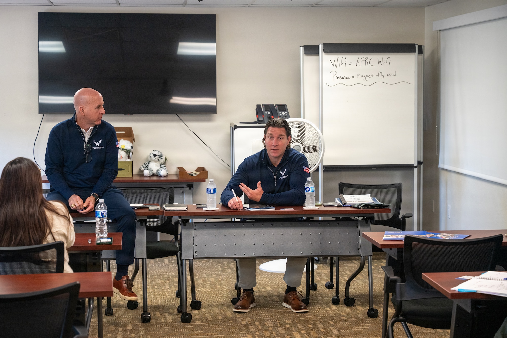 Ed Thomas sits on a table while Packy Lyden talks to military spouses.