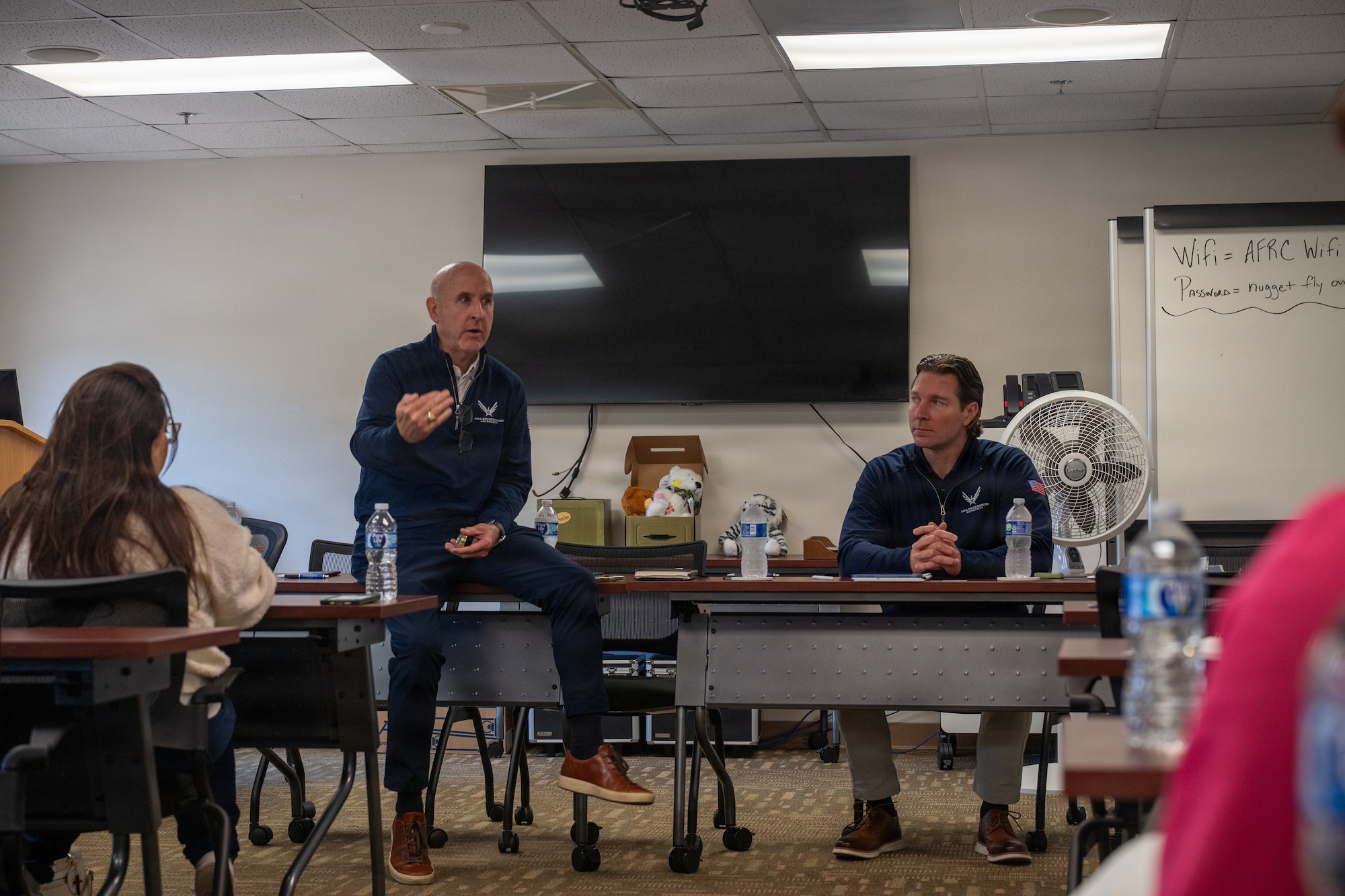 Retired Maj. Gen. Ed Thomas, Air and Space Forces Aid Society chief executive officer talks to Key Spouse Liaisons while sitting on a desk.