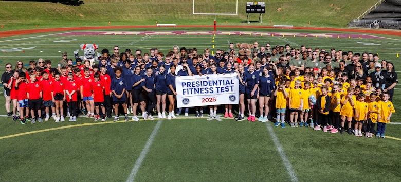 Students from Marine Corps Base Quantico’s Department of War Education Activity schools, U.S. Marines, and staff, pose for a group photo during the Presidential Fitness Test at Butler Stadium on MCB Quantico, Virginia, May 12, 2026. The Presidential Fitness Test consists of three fitness components that are designed to strengthen health, physical fitness, resilience, and establish lifelong healthy habits. The PFT also recognizes multiple levels of achievements, including the Presidential Fitness Award, National Fitness Award, Completion recognition and improvement. (U.S. Marine Corps photo by Lance Cpl. Lynsee Avila-Ramirez)