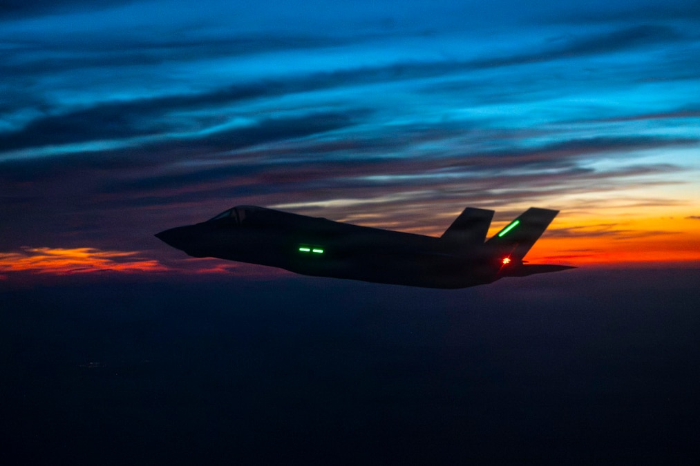 An aircraft flies in a dark blue and orange sky.