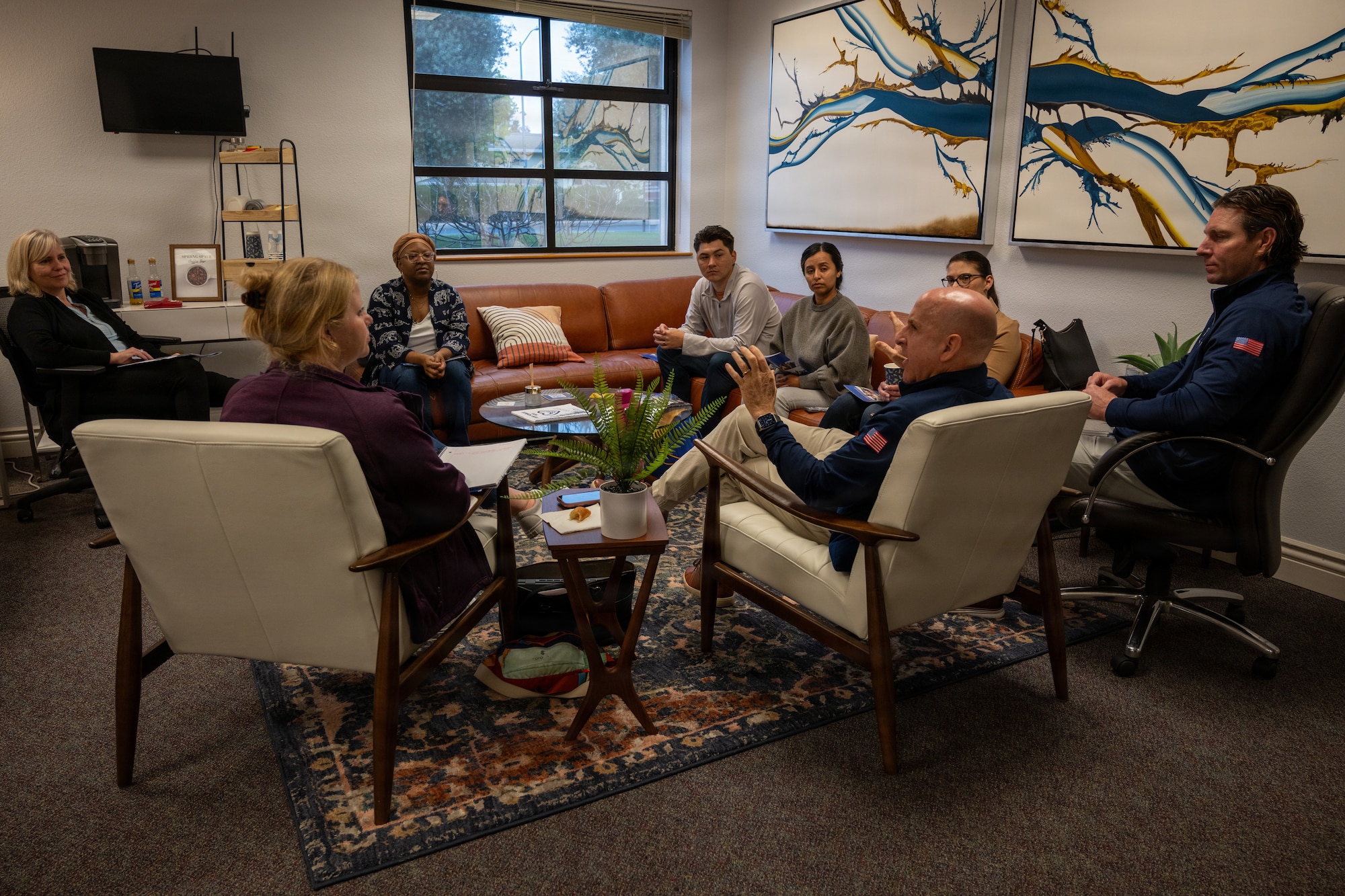 a group of people sitting on a couch and chairs talking to each other
