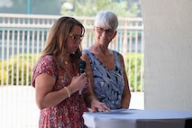 Erin Larsen holds a microphone and gives a speech while Lorraine Larsen stands beside her.