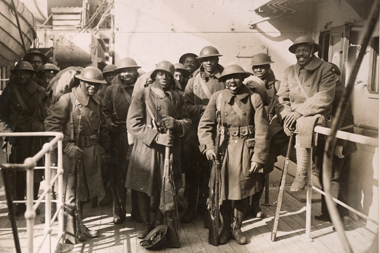 Men wearing military uniforms and holding long guns pose for a group photo aboard a ship.