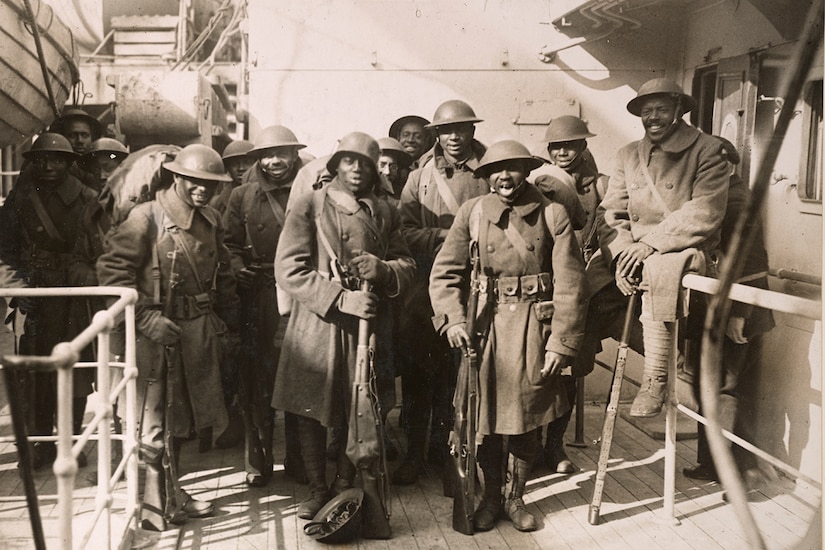 Men wearing military uniforms and holding long guns pose for a group photo aboard a ship.