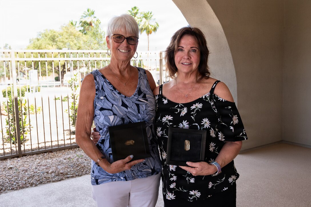 Lorraine Larsen and Suzanne Huberth stand side by side and hold their brother's ID tags posed for a photo.