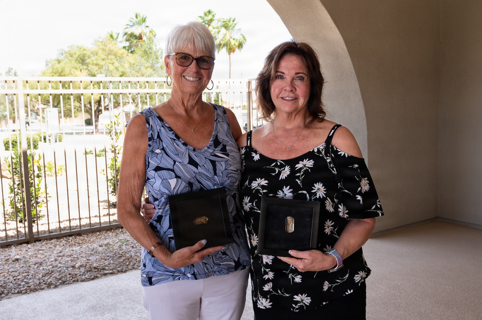 Lorraine Larsen and Suzanne Huberth stand side by side and hold their brother's ID tags posed for a photo.