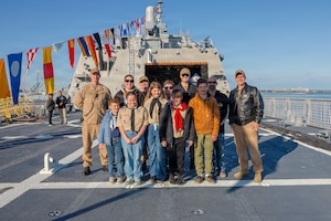 Children and three adults pose for a photo while standing on the deck of a ship.
