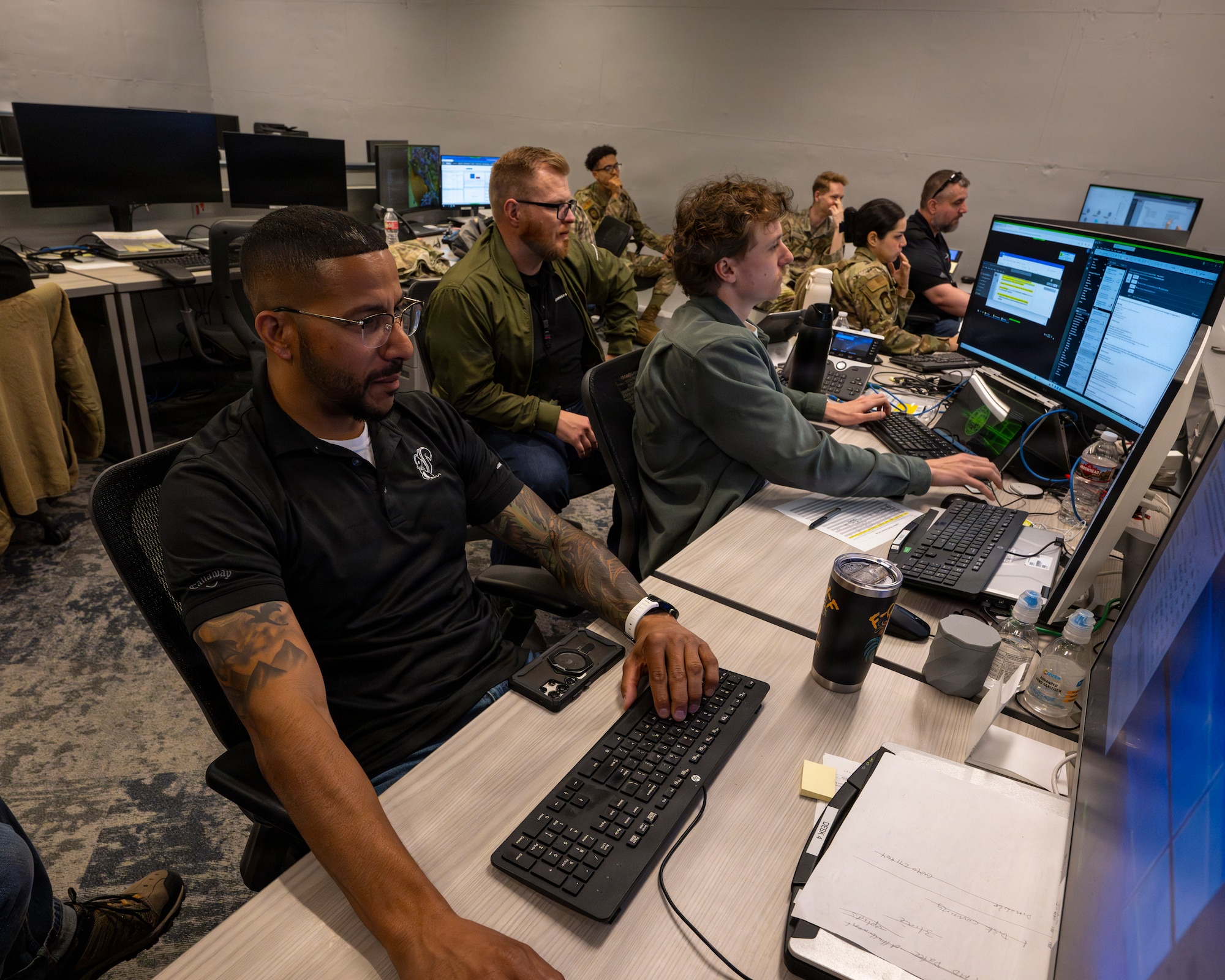 A photo of a group of Airmen and civilians working in a room filled with computers