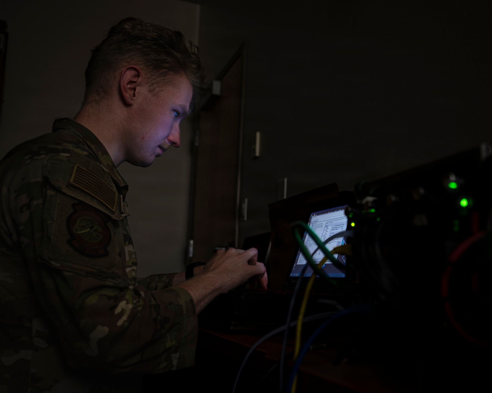 A photo of an Airman in front of a computer screen in a dark room