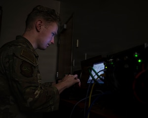 A photo of an Airman in front of a computer screen in a dark room