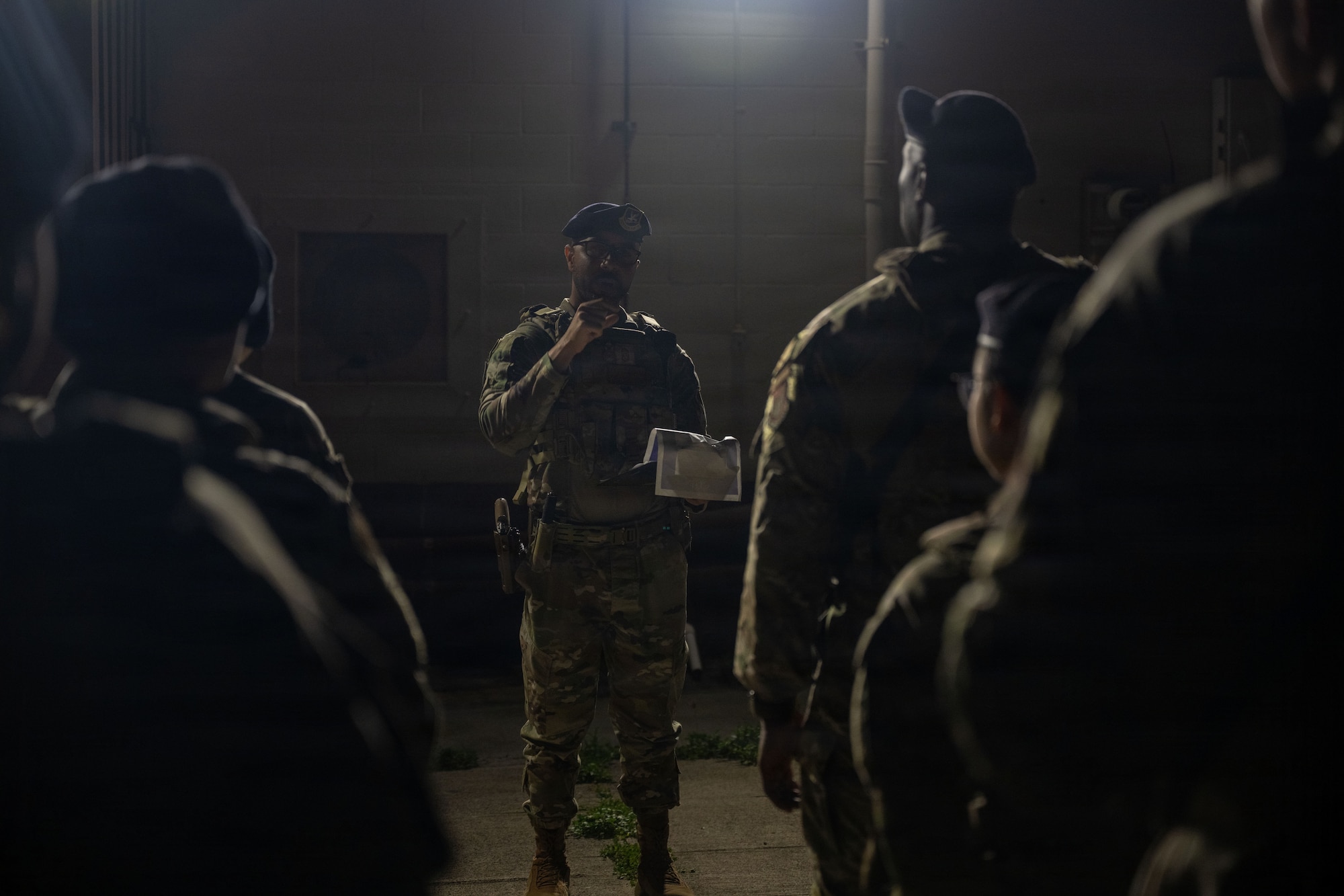 U.S. Air Force Airman holds a checklist while briefing several other Airman outside during the dark of night.