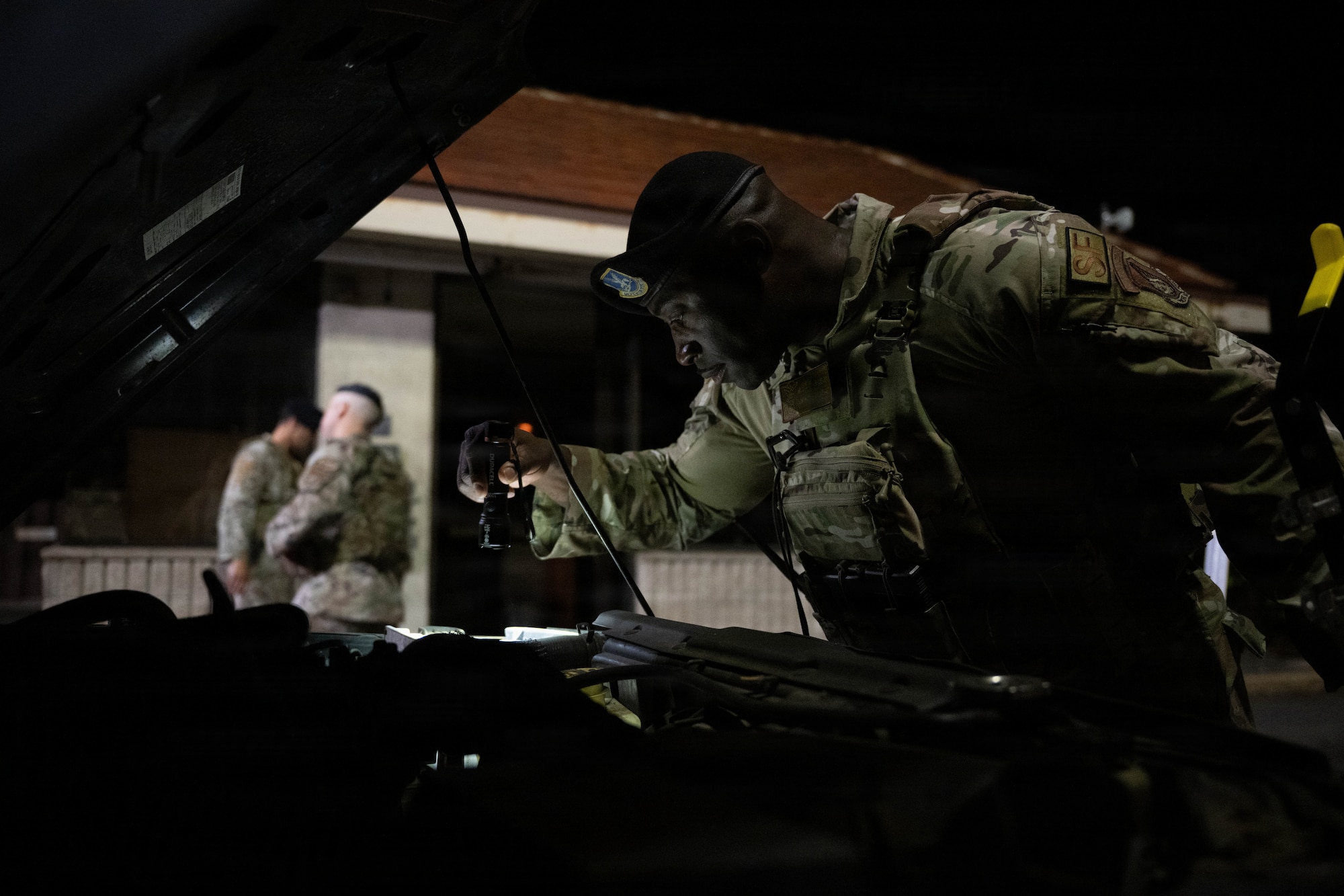U.S. Air Force Airmen checks inside the engine bay of a car passing through a security checkpoint.