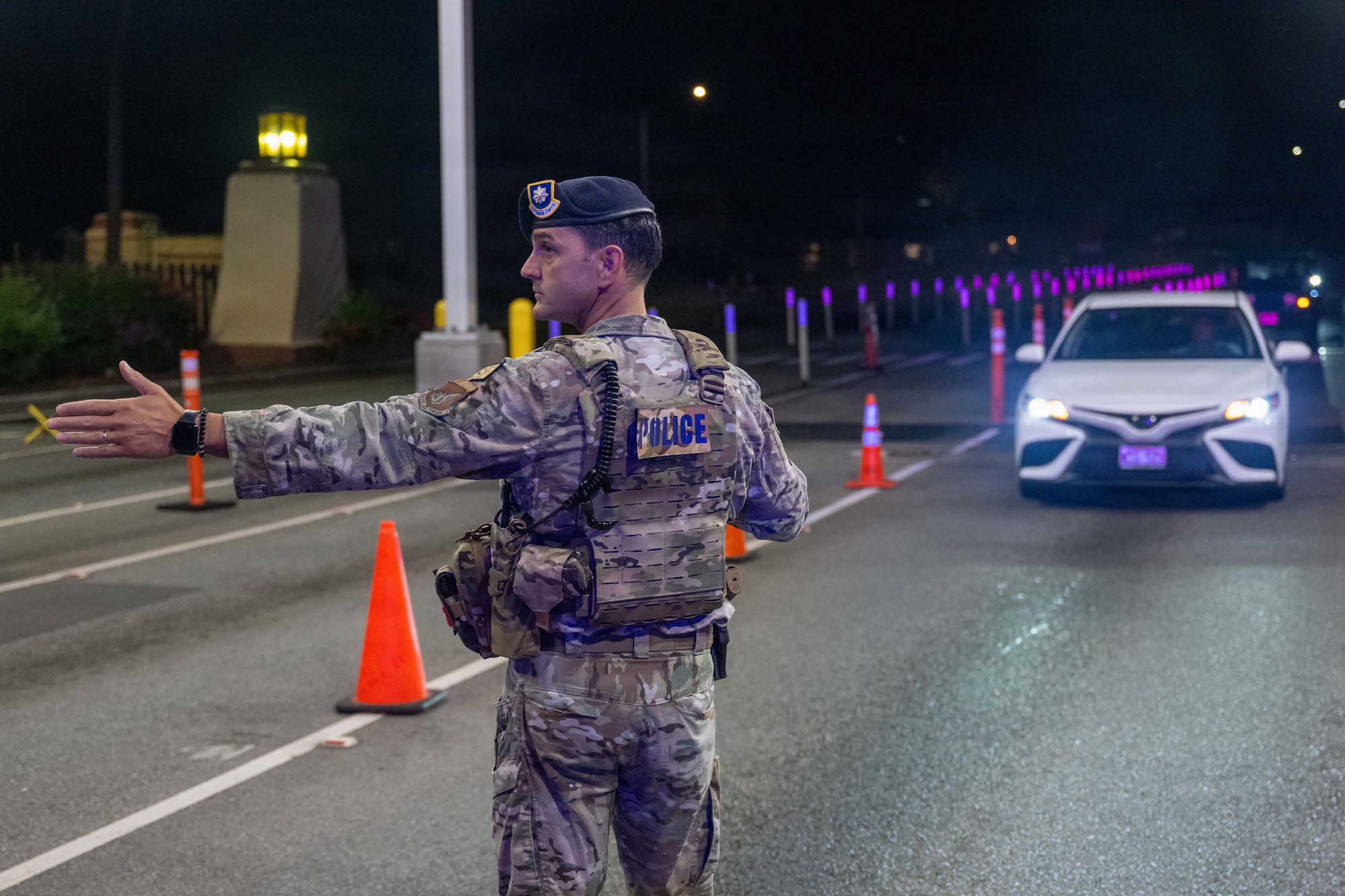 Military Police member holds his hand out to signal a car at night to stop while at the base entrance.