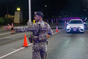 Military Police member holds his hand out to signal a car at night to stop while at the base entrance.