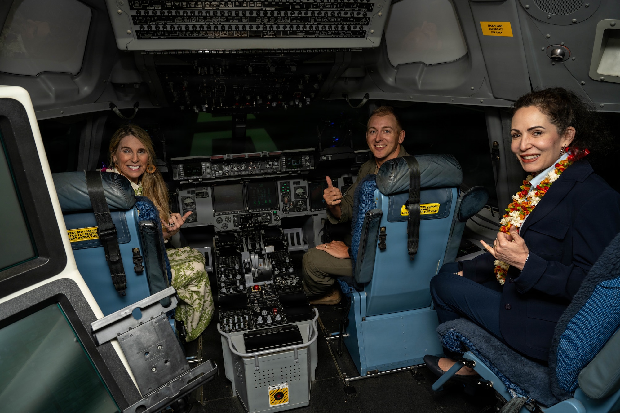 3 people sit in a training cockpit of an aircraft.