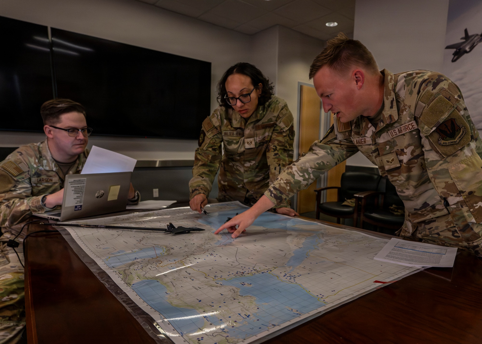 A photo of three Airmen surrounding a map laid out on a table. One of them is pointing something out to the others.