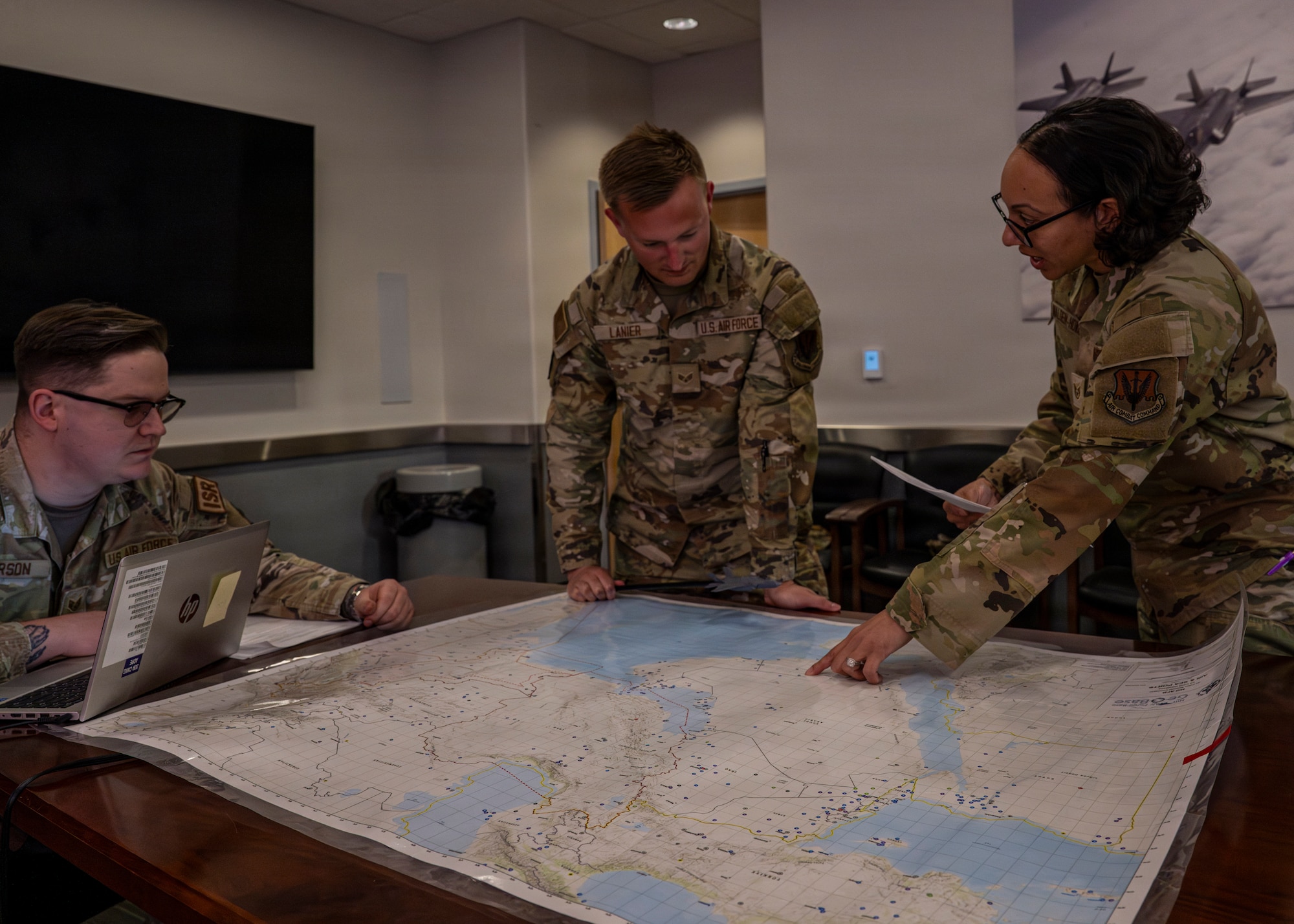 A photo of three Airmen surrounding a map laid out on a table. One of them is pointing something out to the others.