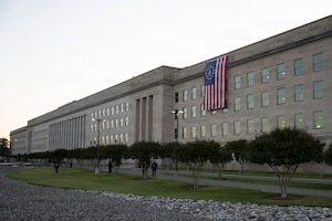 A large American flag hangs off the side of a large, five-story building.