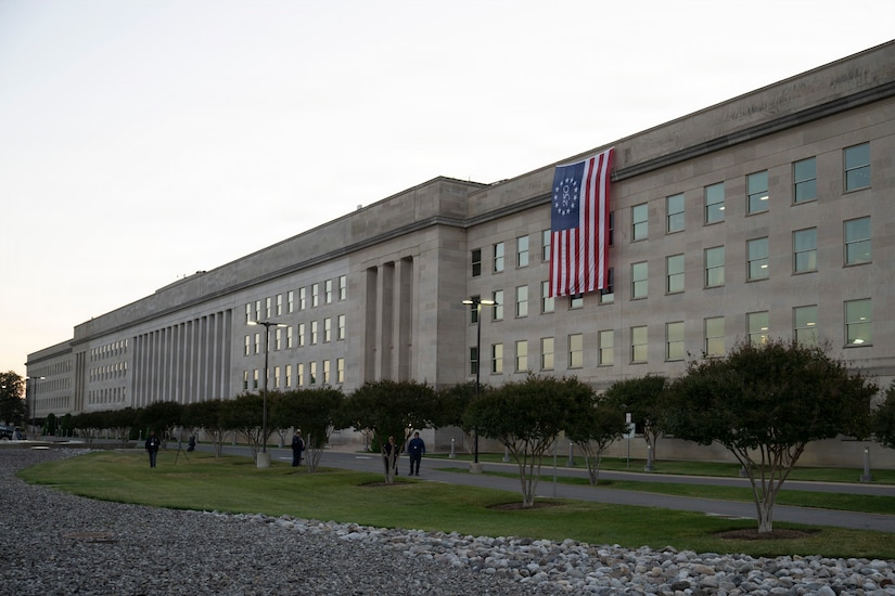 A large American flag hangs off the side of a large, five-story building.