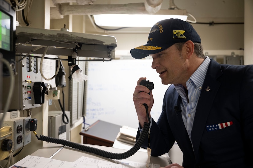 Secretary of War Pete Hegseth speaks into a communication device on a ship.