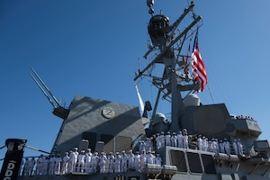 Sailors in white uniforms man the rails of a ship.