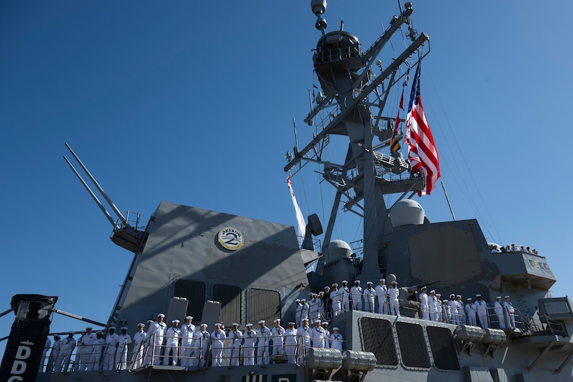 Sailors in white uniforms man the rails of a ship.