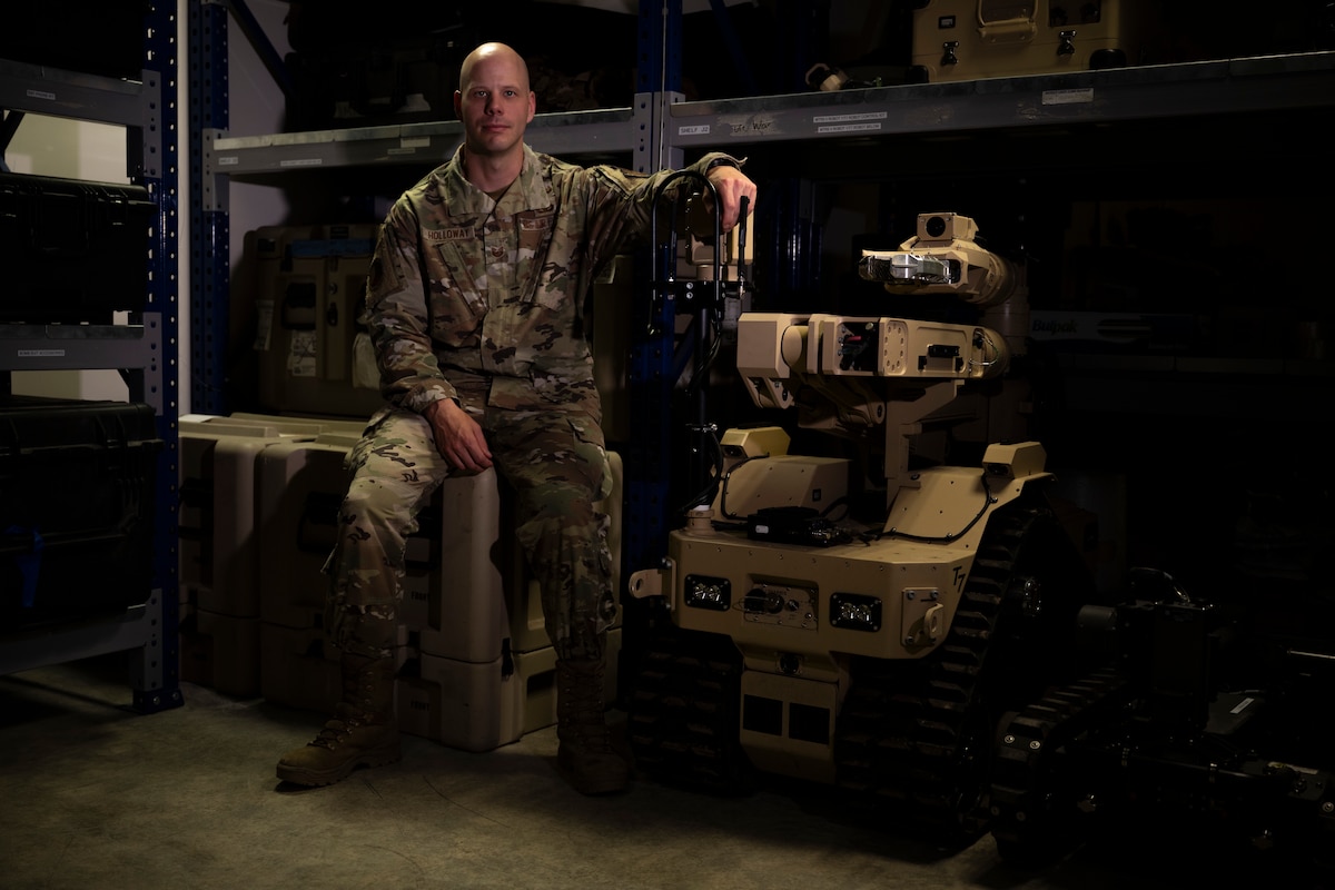 A male military service member posing next to a robot.