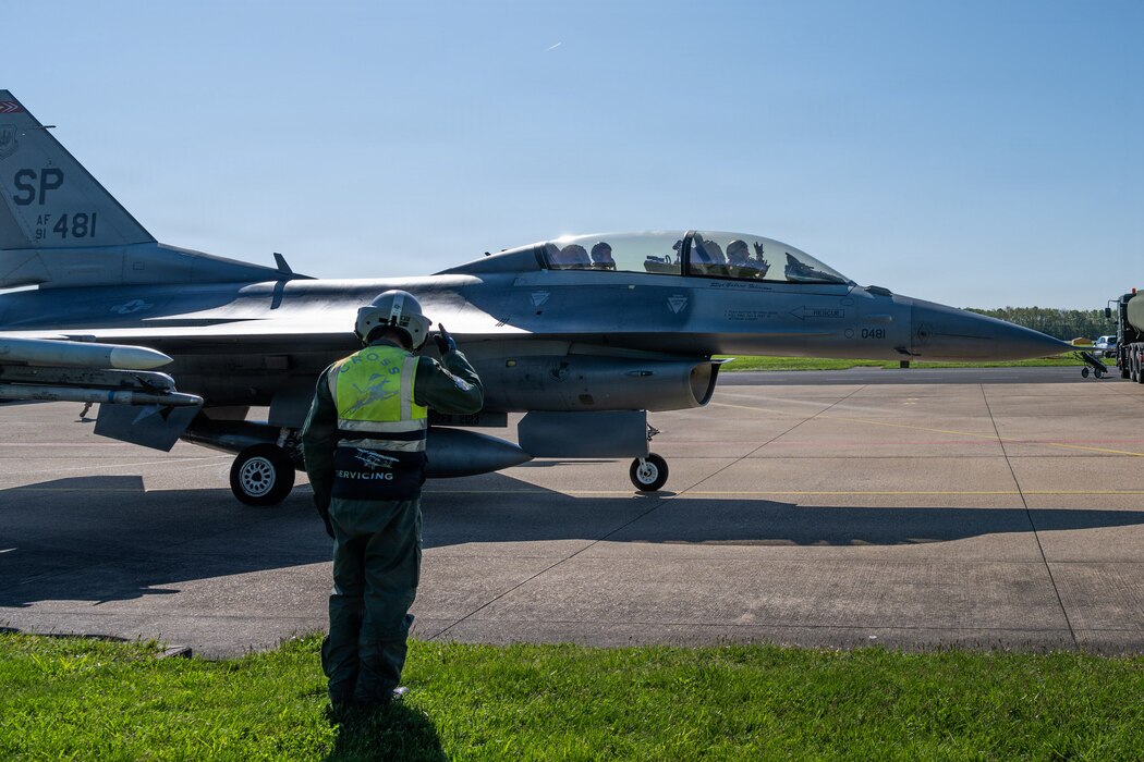 A person salutes an aircraft as it taxis away.