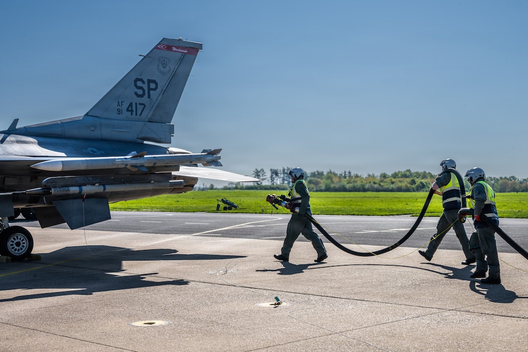 A group of people carry a fuel hose towards an aircraft.