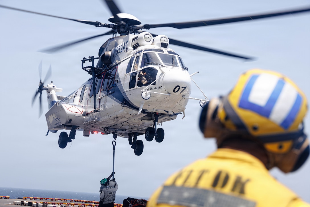 U.S. Sailors embarked aboard the forward-deployed amphibious assault ship USS Tripoli (LHA 7), attach supplies to an EC-255 Super Puma, assigned to the Maritime Pre-Positioning Force, during a vertical replenishment evolution in the U.S. Central Command area of responsibility, May 10, 2026. Tripoli is deployed to the U.S. 5th Fleet area of operations to support maritime security and stability in the Middle East. (U.S. Marine Corps photo)