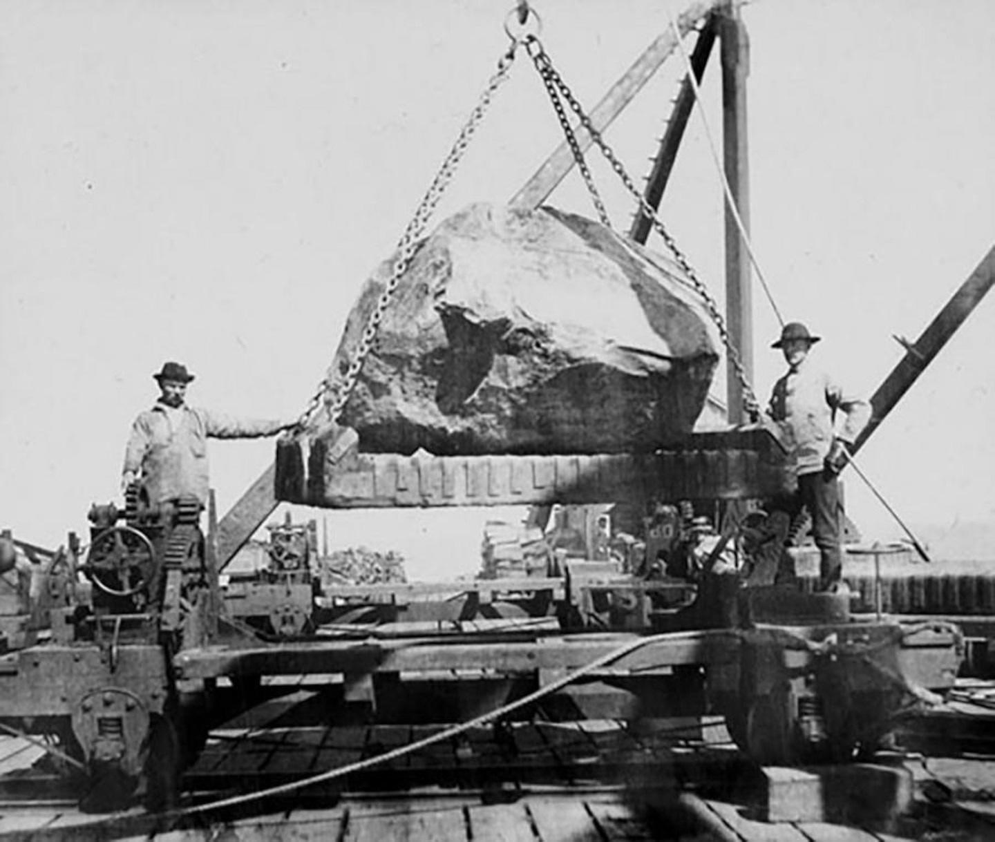 Image of men standing in front of a giant stone placed on a crane.