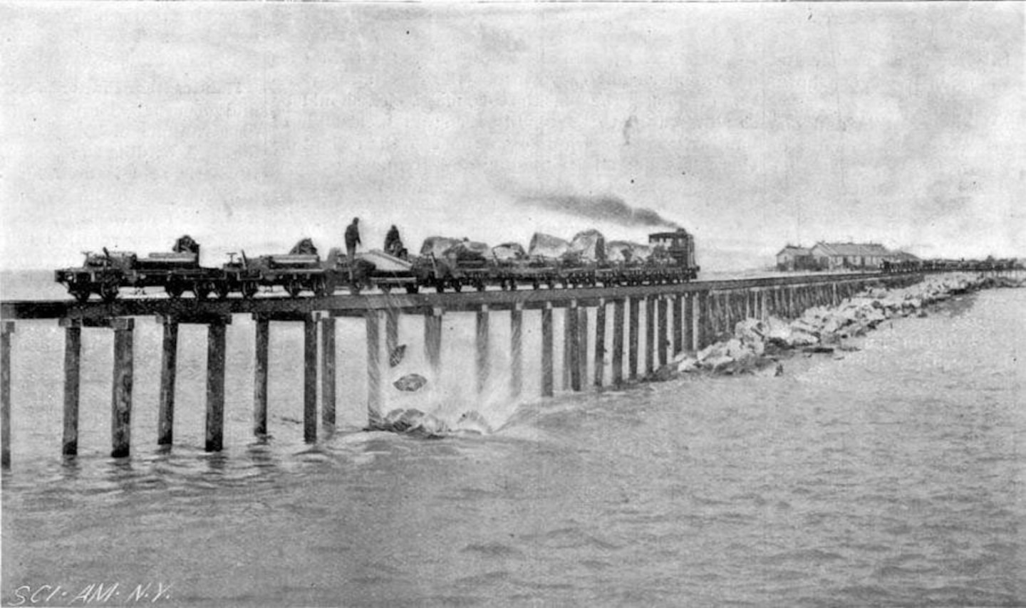 Image of a steam locomotive traveling over a timber trestle over a body of water.