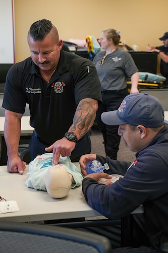 an EMT holds two fingers to an infant-sized CPR dummy as he practices infant chest compressions