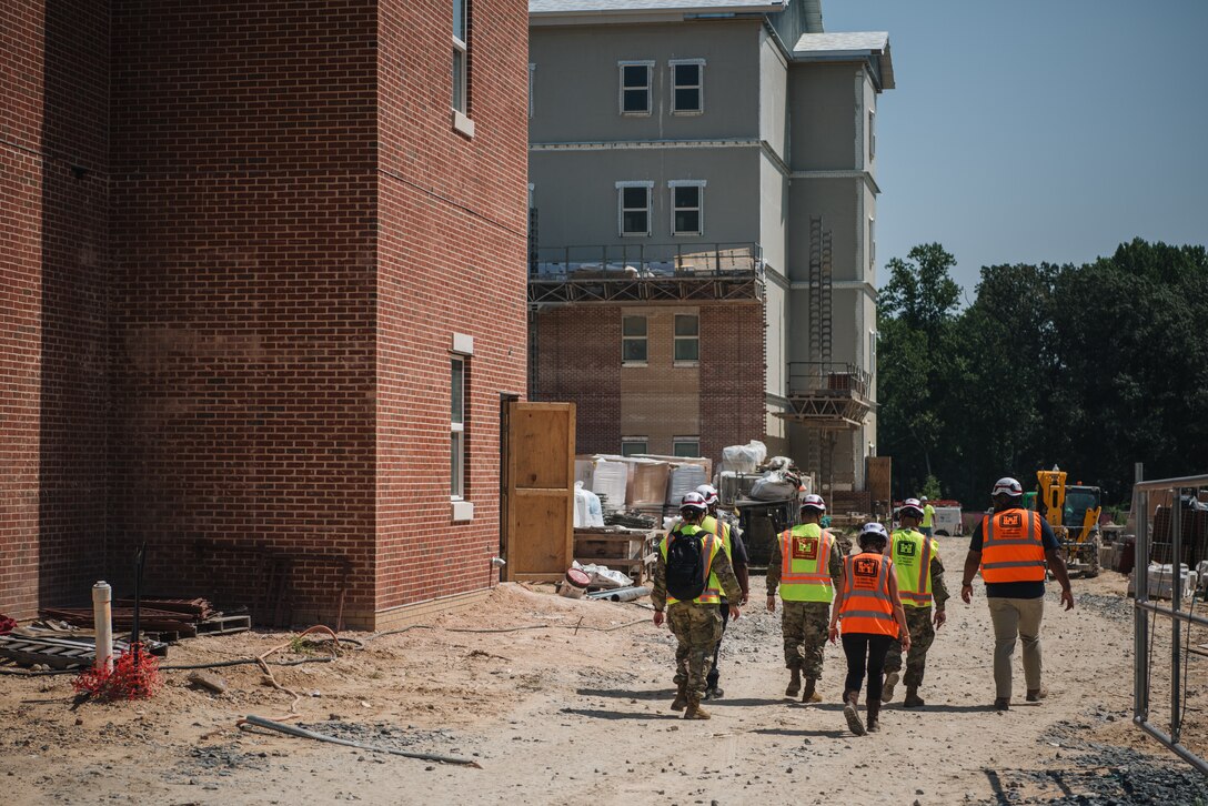 A group of people in hard hats and reflective vests walk near a building under construction
