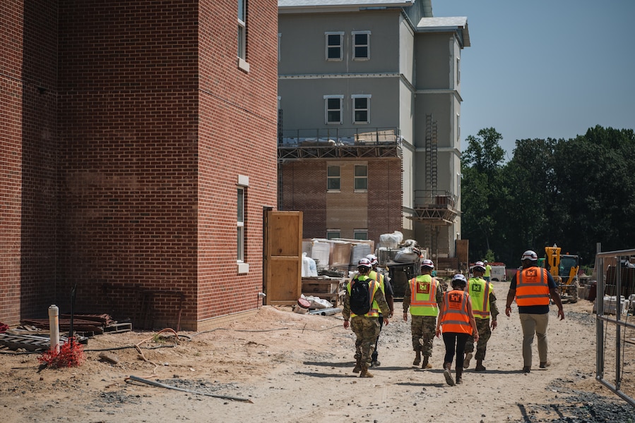 A group of people in hard hats and reflective vests walk near a building under construction