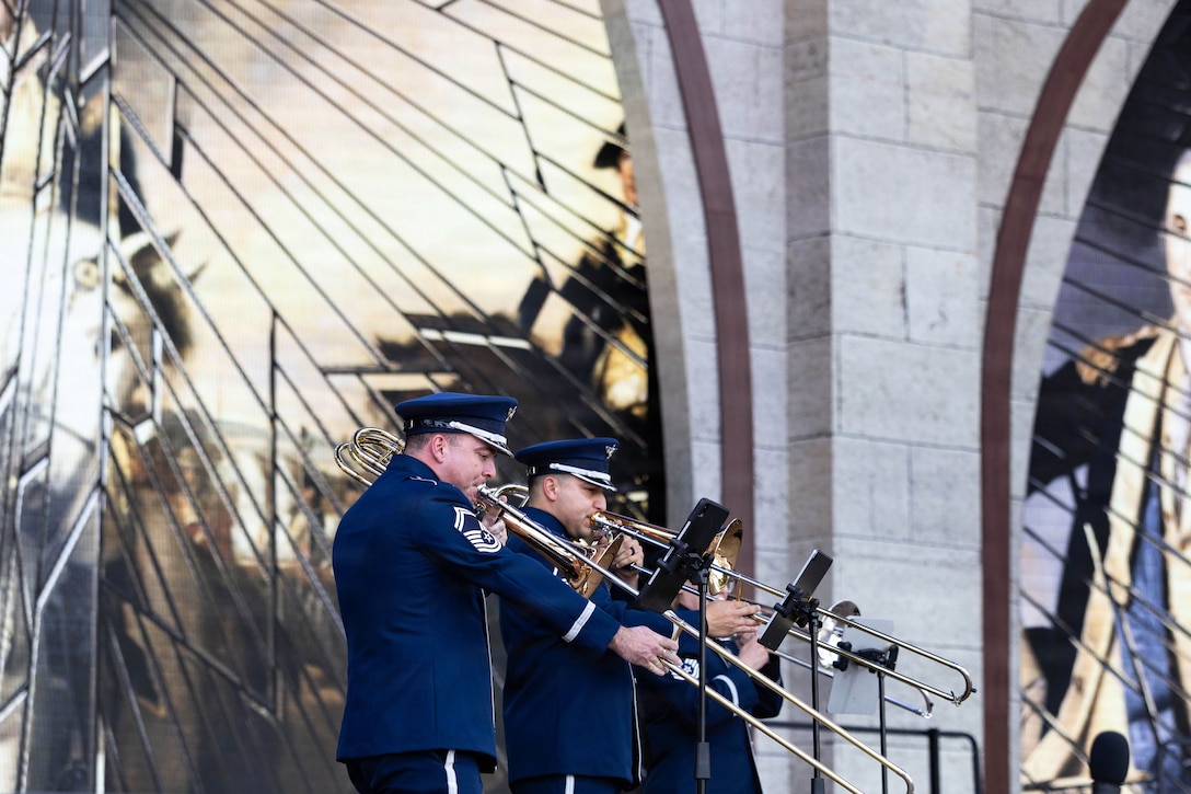 A side view of four airmen in ceremonial dress playing instruments in front of a mirrored building.