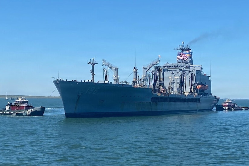 Two tugboats in a body of water guide a large ship into port.