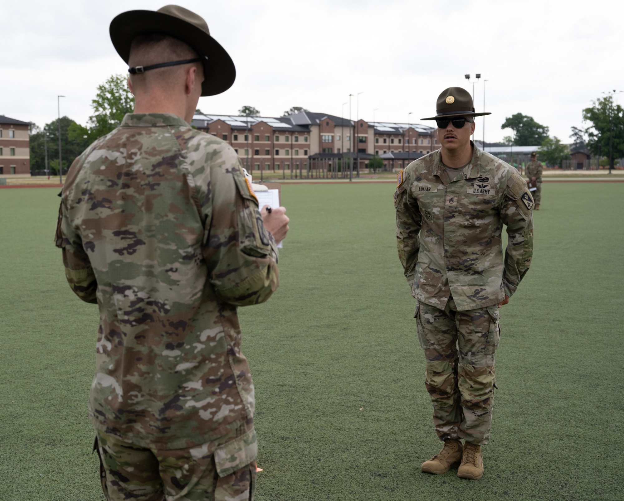 A man stands at the position of attention in front of another man.