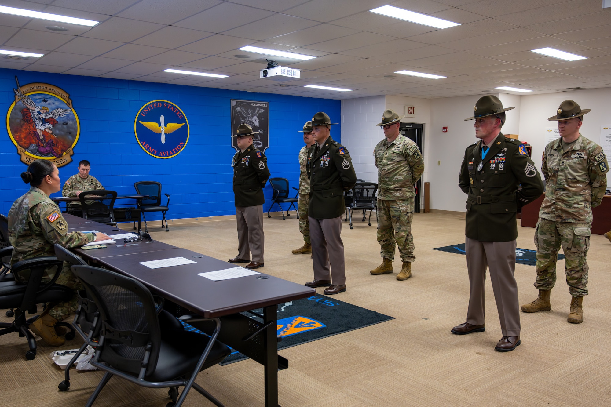 A group of men stand in front of a person sitting at a table.