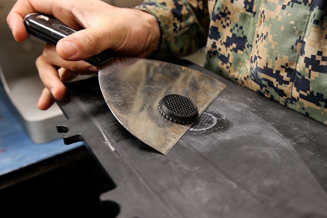 A Marine removes a 3D printed honeycomb fixture from a printing plate