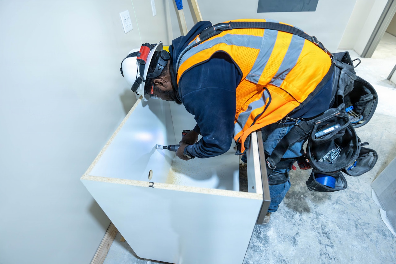A man wearing a safety vest and a helmet installs a cabinet.