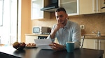 Man in blue shirt sits at a kitchen table and reads a piece of paper