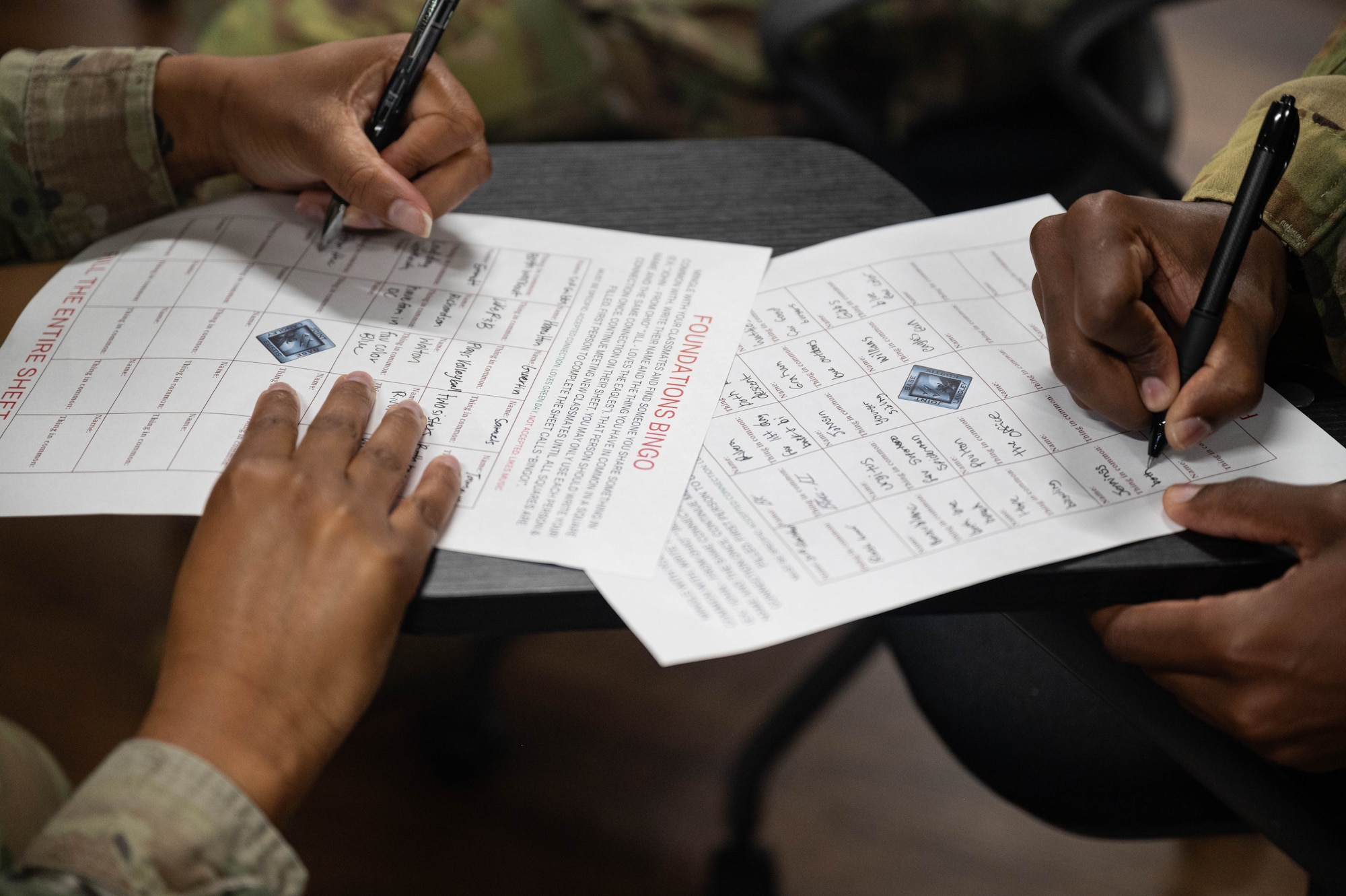 Two U.S. Airmen write on papers at chair desks.