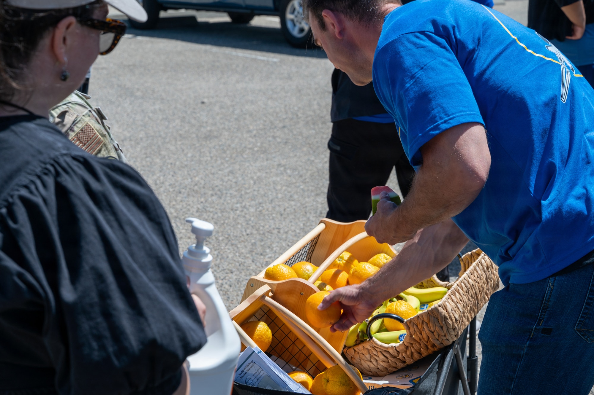 A person reaches for oranges in a basket outside.