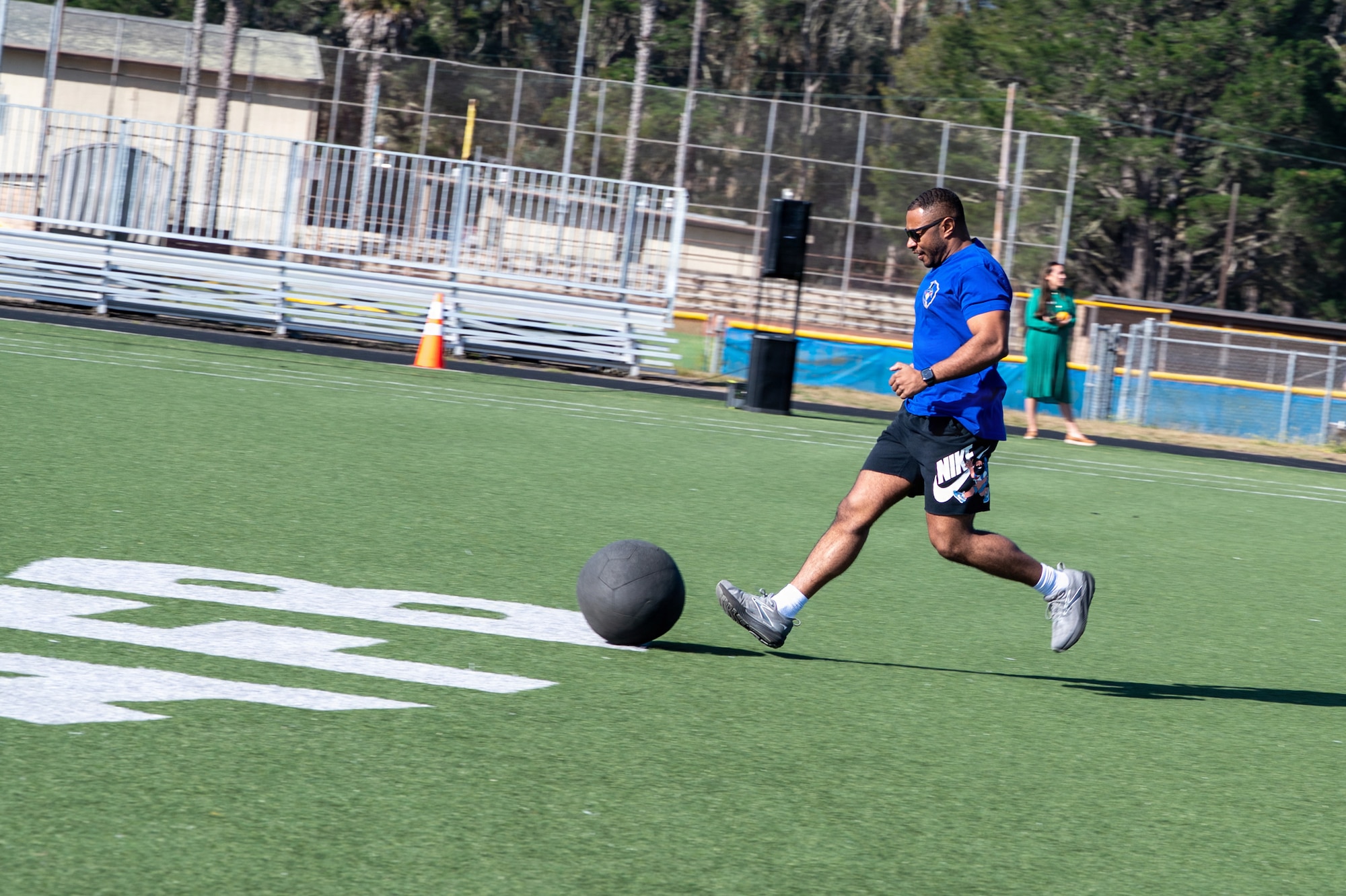 A person runs after a medicine ball on a turf field outside.