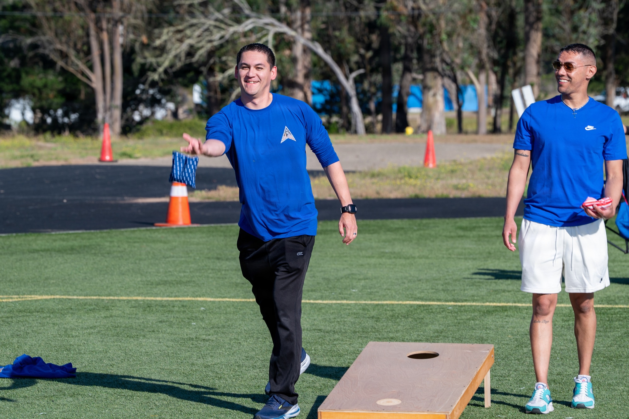 A person tosses a bean bag outside on a turf field.