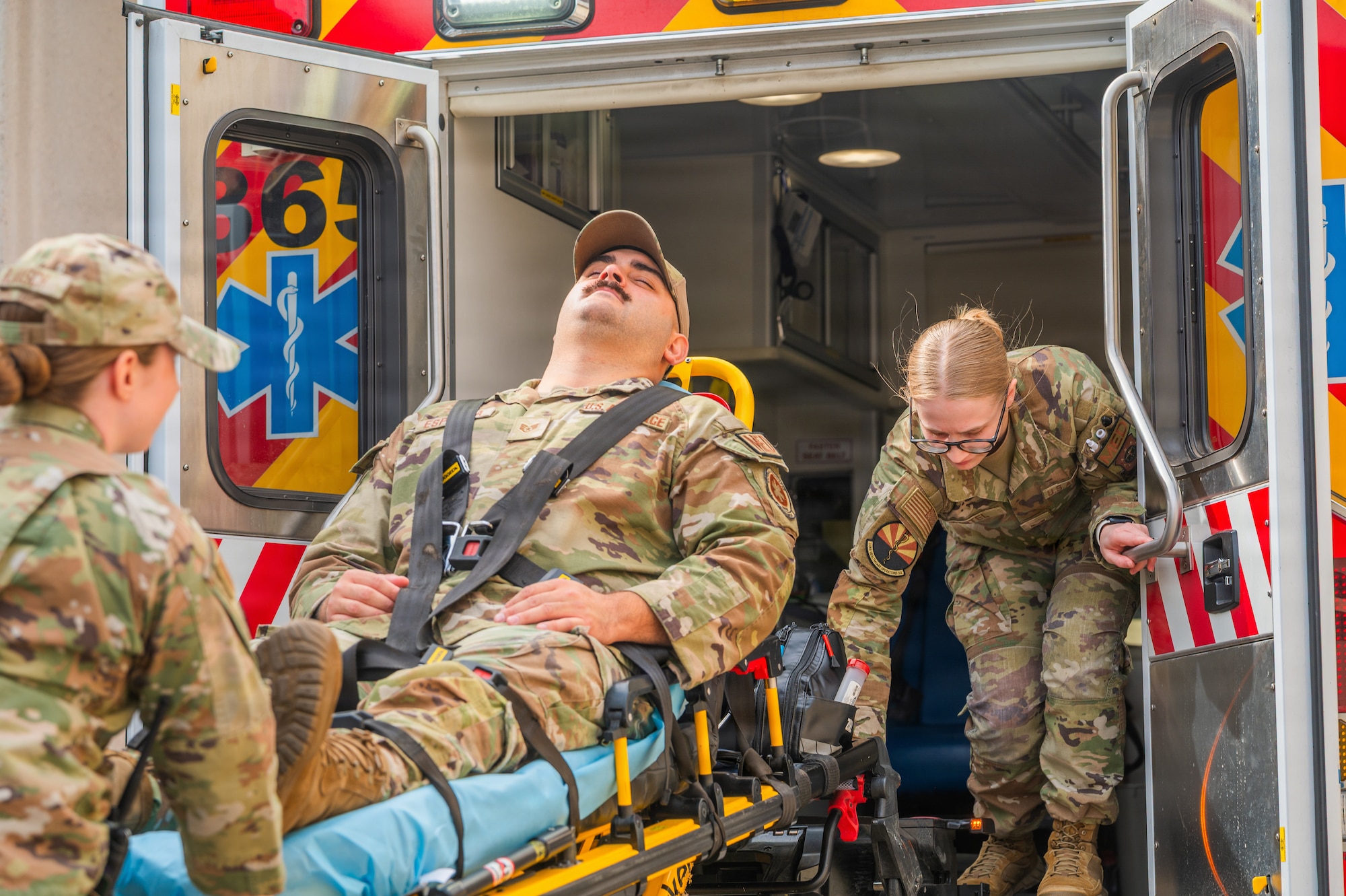 U.S. Air Force Senior Airman Arianna Blaasch, an ambulance services medical technician, left, Staff Sgt. Dominick Espinoza, ambulance services noncommissioned officer in charge, center, and Senior Airman Hannah Martel, an ambulance services medical technician, all assigned to the Luke Medical Group Healthcare Operations Squadron, demonstrate unloading a gurney during training at Luke Air Force Base, Arizona, May 13, 2026.