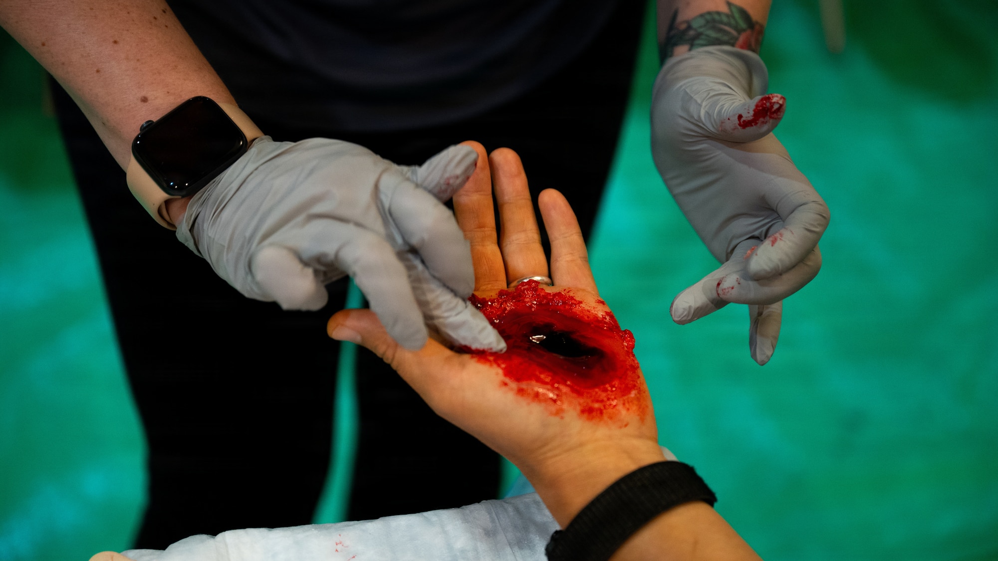 A person wearing gloves applies a bloody wound to the palm of someone's hand.
