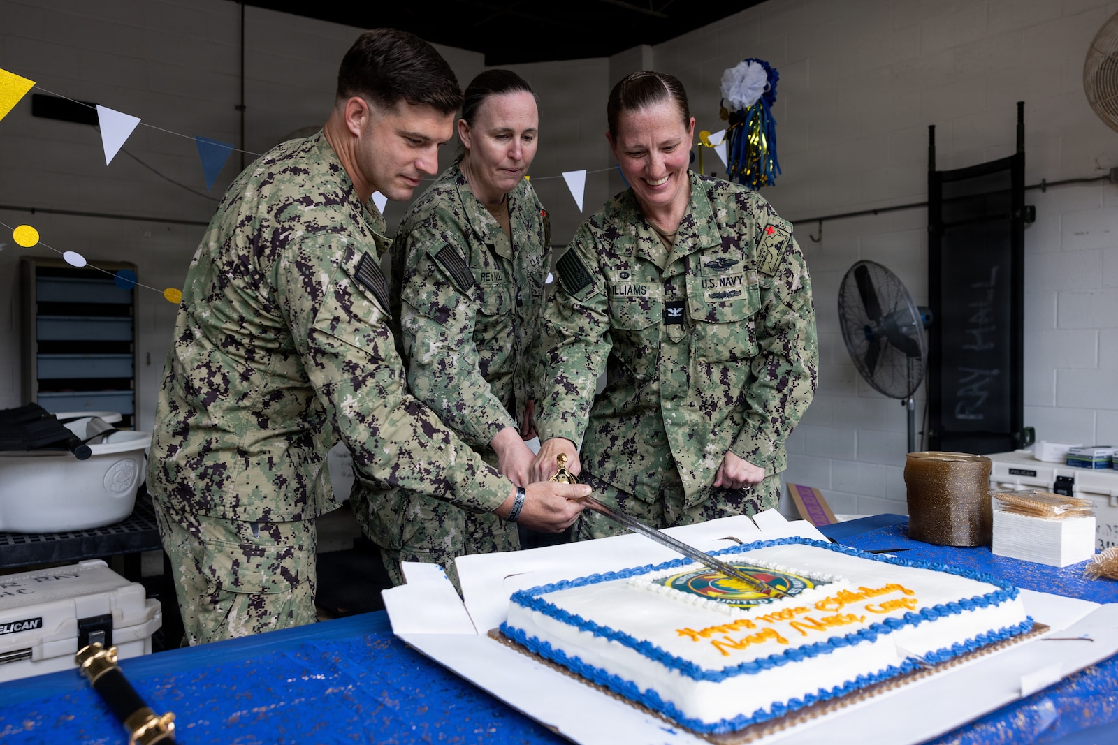 U.S. Navy Lt. Michael Murphy, left, officer in charge of David R. Ray Branch Health Clinic, Capt. Margaret Reynolds, executive officer chief of Navy Medical Readiness Training Command, and Capt. Brookes Williams, commanding officer of Navy Medical Readiness Training Command, cut a cake during the Nurse Appreciation Week cake cutting ceremony at the David R. Ray Branch Health Clinic on Marine Corps Base Quantico, Virginia, May 13, 2026. The cake cutting ceremony reflects on the history of the Nurse Corps and symbolizes the passing of knowledge from the most senior officer to the most junior officer. (U.S. Marine Corps photo by Sgt. Chancellor Reynolds)
