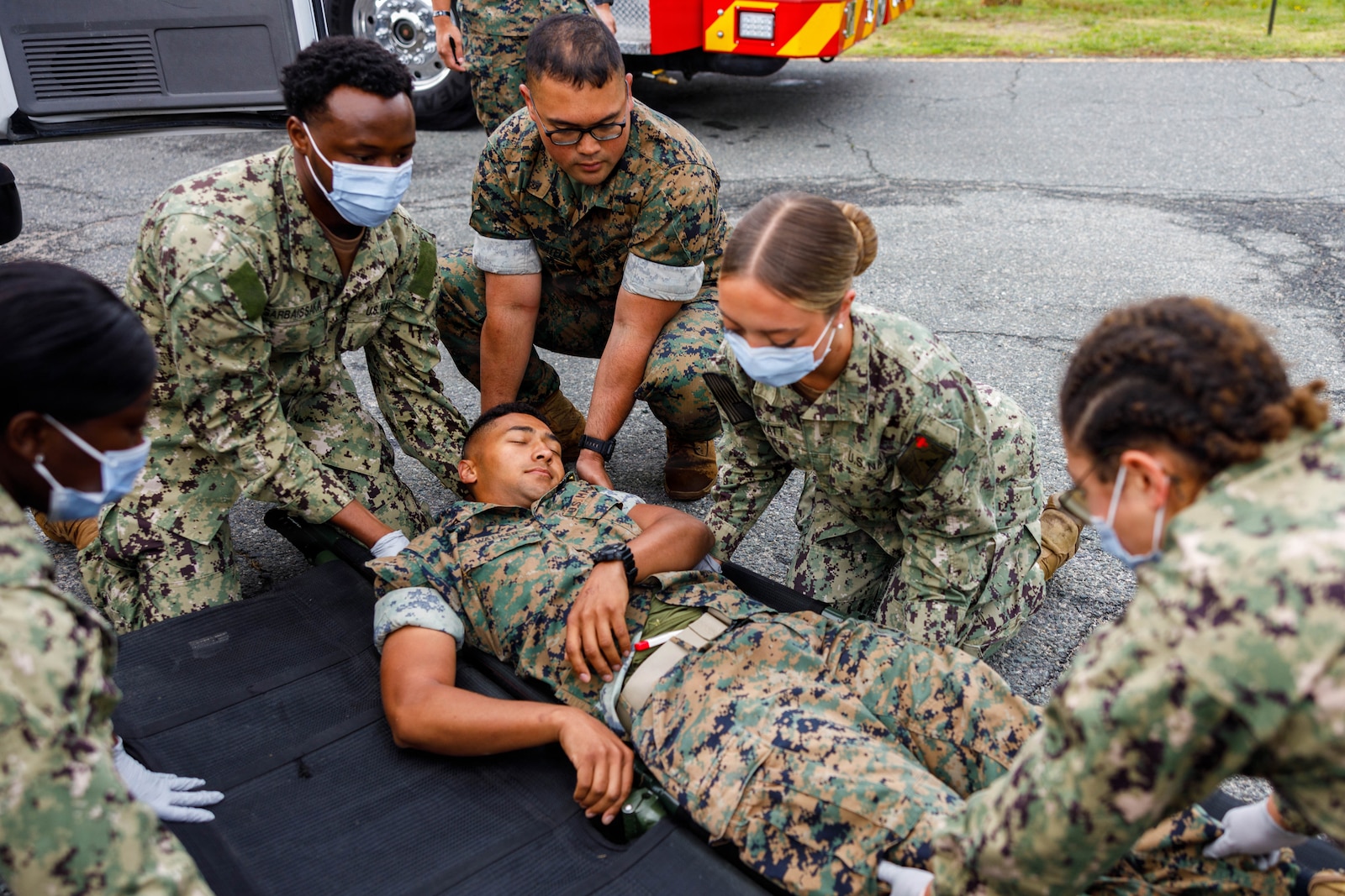 U.S. Marine Corps Lance Cpl. Joshua Walker, a motor vehicle operator with Training Command, lays on a stretcher while U.S. Navy corpsman provide aid during the Mass Casualty Training Event at the Officer Candidate School on Marine Corps Base Quantico, Virginia, May 14, 2026. The Mass Casualty Training Event consists of several different stations with mock casualties that are tended and taken to the main OCS clinic for additional treatment in order to further qualify hospital corpsman. (U.S. Marine Corps photo by Lance Cpl. Lynsee Avila-Ramirez)